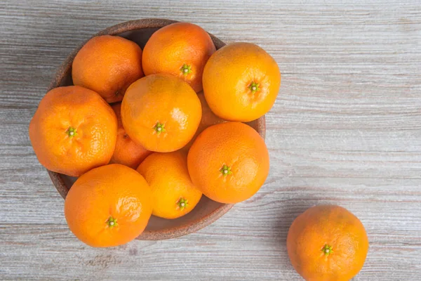 Beyaz desenli ahşap panoda seramik bir kasede bir demet taze portakal..