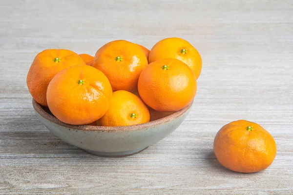 Beyaz desenli ahşap panoda seramik bir kasede bir demet taze portakal..