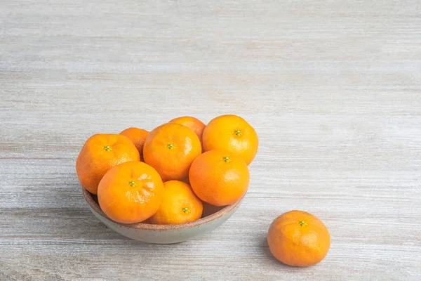 Beyaz desenli ahşap panoda seramik bir kasede bir demet taze portakal..