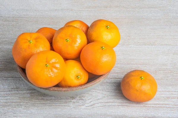 Beyaz desenli ahşap panoda seramik bir kasede bir demet taze portakal..