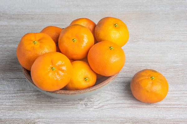 Beyaz desenli ahşap panoda seramik bir kasede bir demet taze portakal..