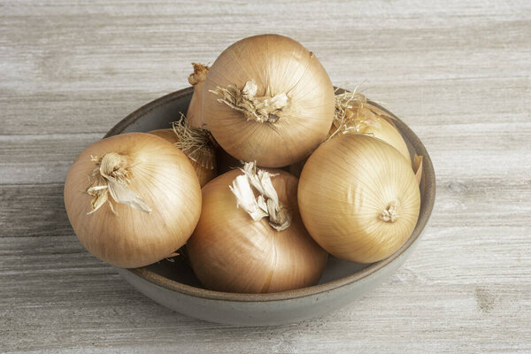 A bunch of authentic southern sweet onions artfully arranged on a ceramic bowl placed on a white painted rustic wood panel board.