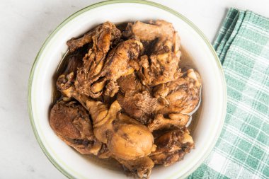Yeşil peçeteli yeşil bir kâse içinde mermer bir masanın üstüne serili Filipin usulü tavuk adobo tabağı..