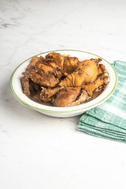 Yeşil peçeteli yeşil bir kâse içinde mermer bir masanın üstüne serili Filipin usulü tavuk adobo tabağı..