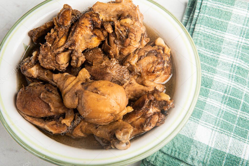 A serving of Filipino-style chicken adobo dish in a bowl with green napkin set on a marble tabletop.