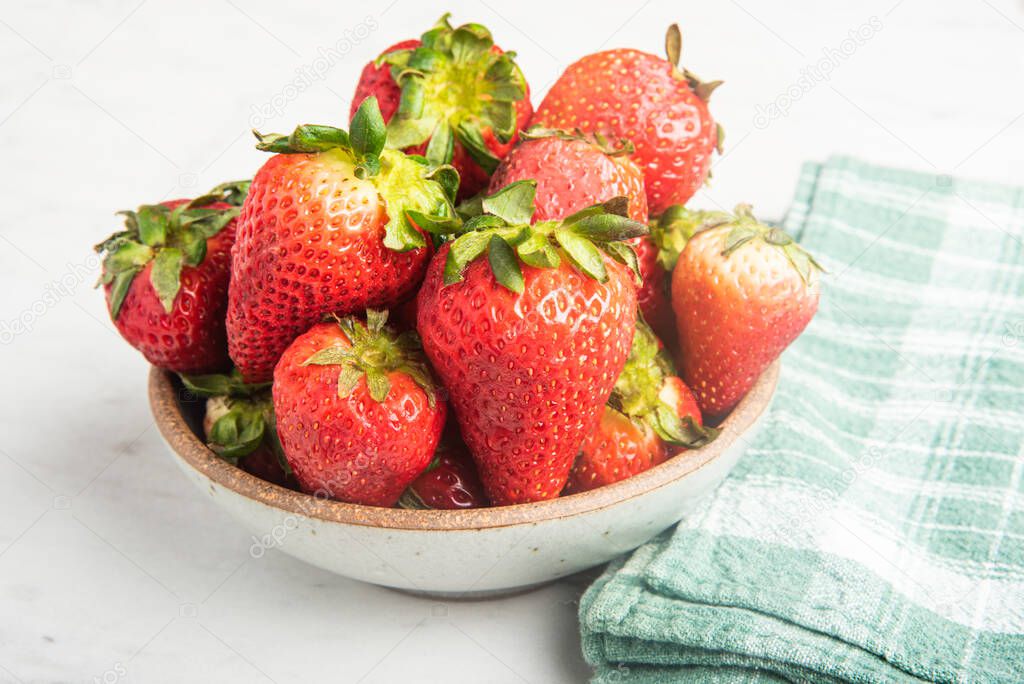 A ceramic bowl of fresh and sweet red strawberries set on a marble countertop with green napkin.