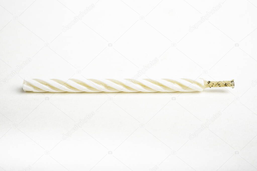 A macro shot of an unlit full birthday cake topping candle with single decorative color swirl set on a plain white background.