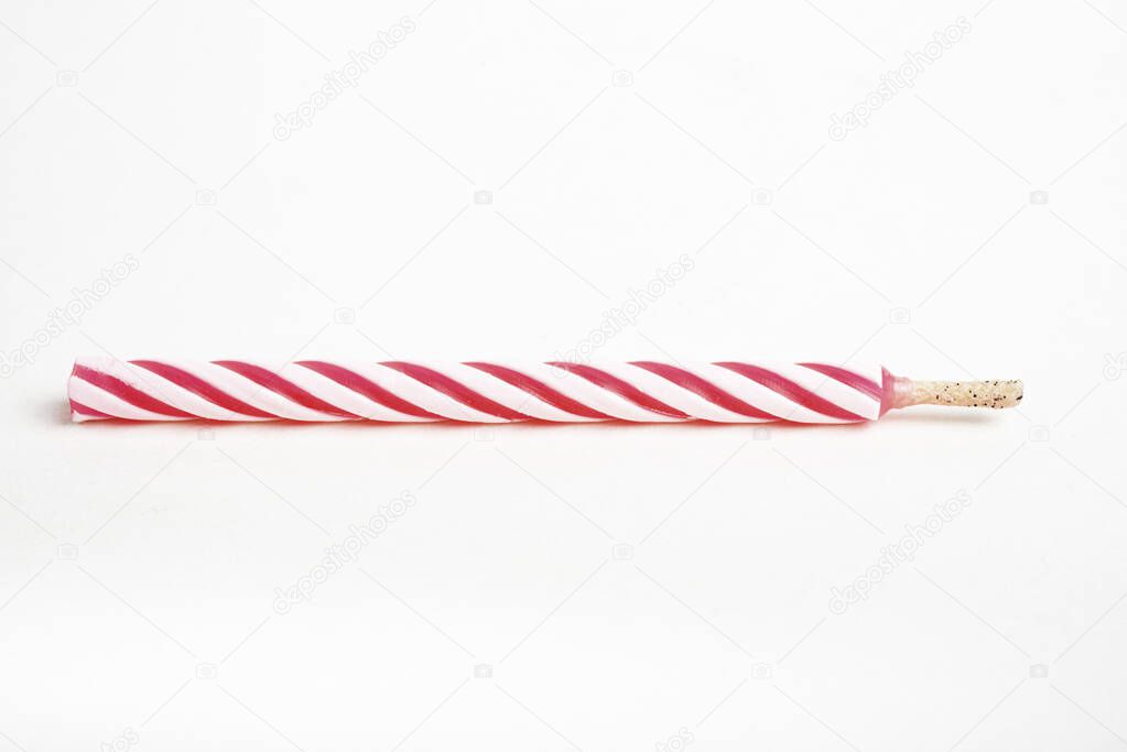 A macro shot of an unlit full birthday cake topping candle with single decorative color swirl set on a plain white background.