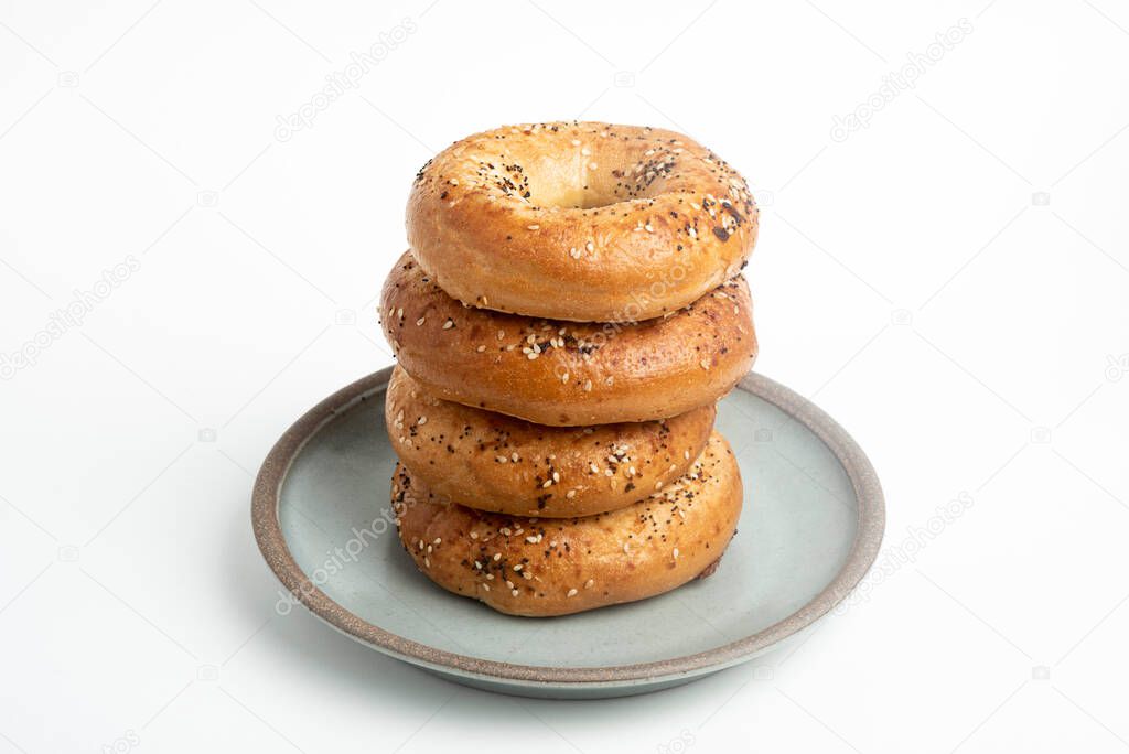 A single tall stack of 4 everything bagels on a ceramic plate set on plain white background. 