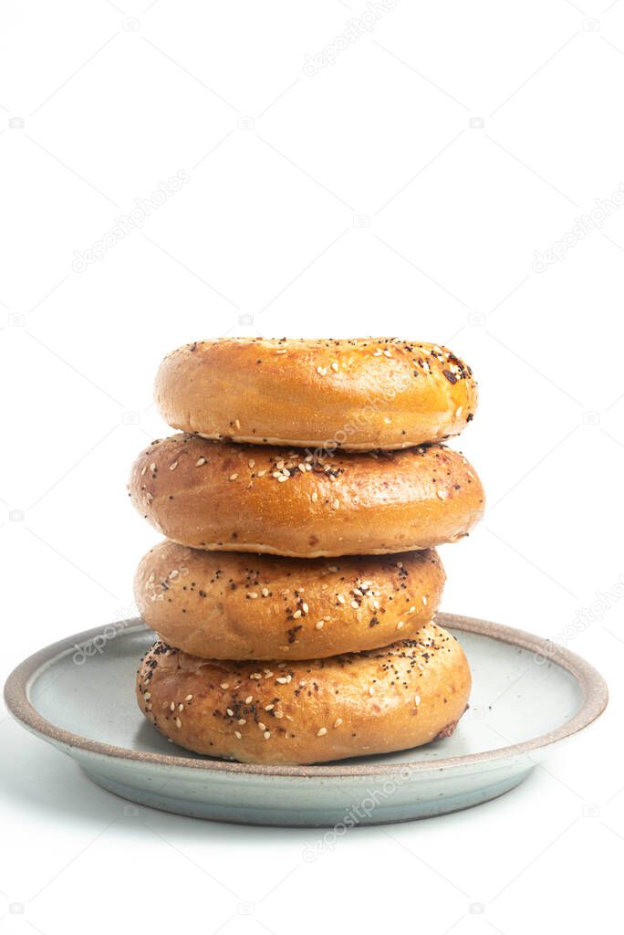A single tall stack of 4 everything bagels on a ceramic plate set on plain white background. 
