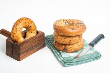 Bir peçetede üç adet yeni pişmiş simit ve tahta kesme tezgahında bir simit ve beyaz arka planda bir bıçak..