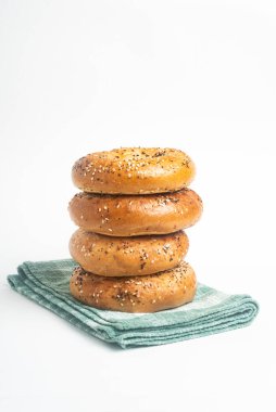 Düz beyaz arka planda yeşil bir peçete seti üzerinde dört adet yeni pişmiş simit yığını..