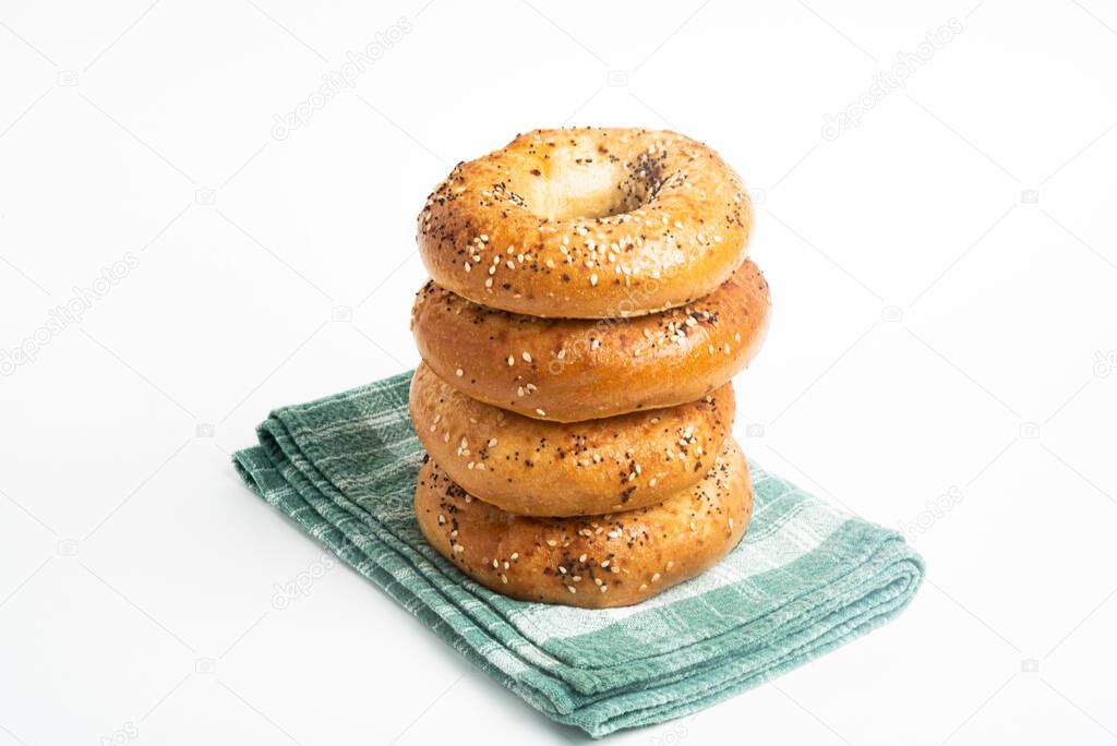 A single tall stack of four freshly baked bagels on a green napkin set on a plain white background.