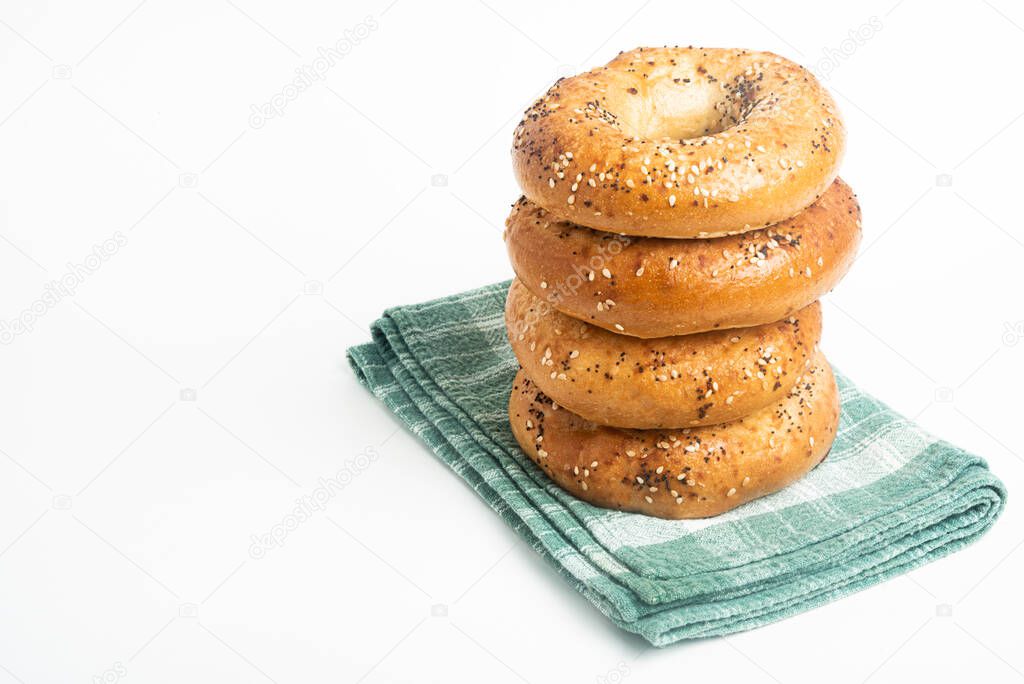 A single tall stack of four freshly baked bagels on a green napkin set on a plain white background.