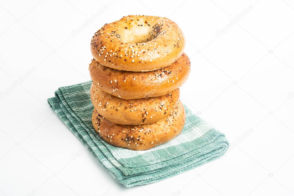 A single tall stack of four freshly baked bagels on a green napkin set on a plain white background.