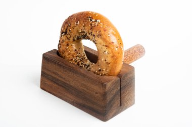 Düz beyaz bir zemin üzerinde ahşap dilimleme tezgahında duran taze pişmiş tek bir simit..