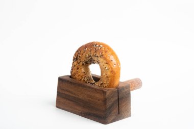 Düz beyaz bir zemin üzerinde ahşap dilimleme tezgahında duran taze pişmiş tek bir simit..