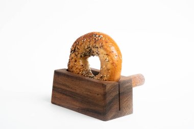 Düz beyaz bir zemin üzerinde ahşap dilimleme tezgahında duran taze pişmiş tek bir simit..