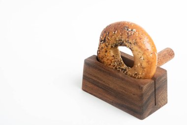 Düz beyaz bir zemin üzerinde ahşap dilimleme tezgahında duran taze pişmiş tek bir simit..