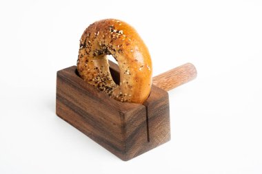 Düz beyaz bir zemin üzerinde ahşap dilimleme tezgahında duran taze pişmiş tek bir simit..