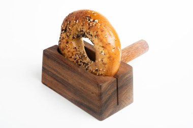 Düz beyaz bir zemin üzerinde ahşap dilimleme tezgahında duran taze pişmiş tek bir simit..