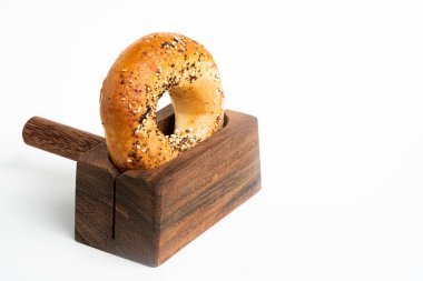 Düz beyaz bir zemin üzerinde ahşap dilimleme tezgahında duran taze pişmiş tek bir simit..