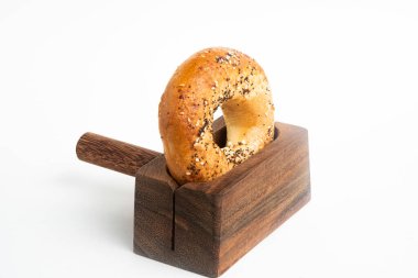 Düz beyaz bir zemin üzerinde ahşap dilimleme tezgahında duran taze pişmiş tek bir simit..