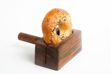 Düz beyaz bir zemin üzerinde ahşap dilimleme tezgahında duran taze pişmiş tek bir simit..