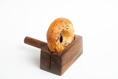 Düz beyaz bir zemin üzerinde ahşap dilimleme tezgahında duran taze pişmiş tek bir simit..