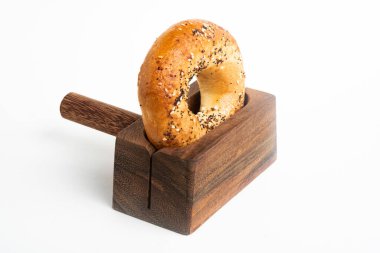 Düz beyaz bir zemin üzerinde ahşap dilimleme tezgahında duran taze pişmiş tek bir simit..