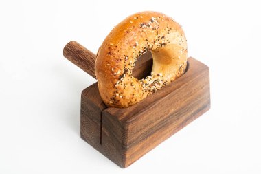 Düz beyaz bir zemin üzerinde ahşap dilimleme tezgahında duran taze pişmiş tek bir simit..