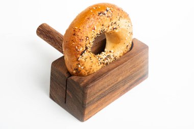 Düz beyaz bir zemin üzerinde ahşap dilimleme tezgahında duran taze pişmiş tek bir simit..