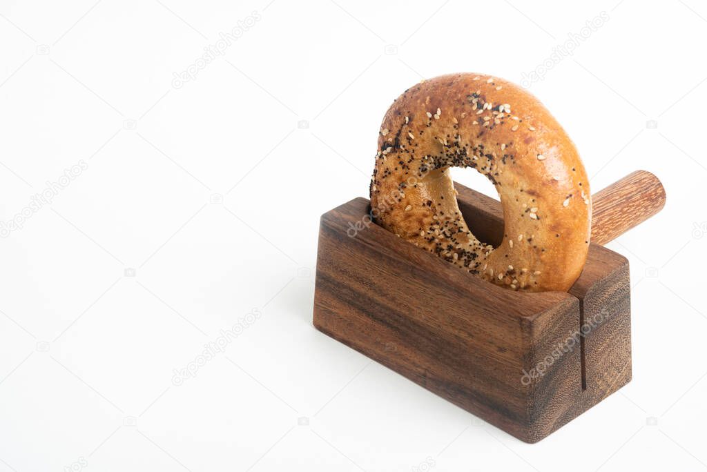 A single freshly baked bagel propped on a wood slicing stand set on a plain white background.