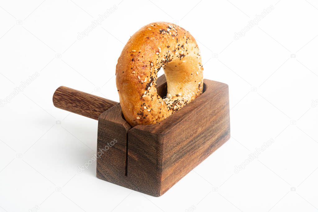 A single freshly baked bagel propped on a wood slicing stand set on a plain white background.