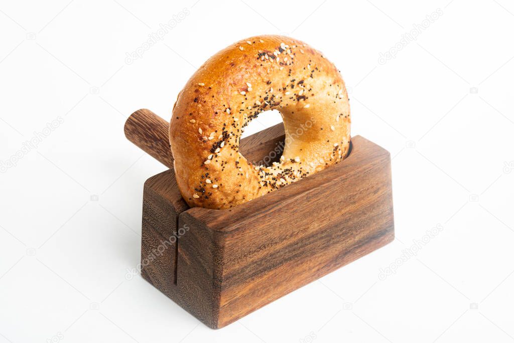 A single freshly baked bagel propped on a wood slicing stand set on a plain white background.