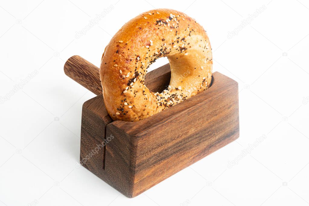 A single freshly baked bagel propped on a wood slicing stand set on a plain white background.