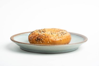 Beyaz arka planda seramik tabakta taze pişmiş tek bir simit..