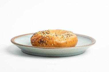 Beyaz arka planda seramik tabakta taze pişmiş tek bir simit..