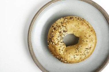 Beyaz arka planda seramik tabakta taze pişmiş tek bir simit..