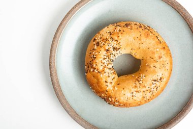 Beyaz arka planda seramik tabakta taze pişmiş tek bir simit..