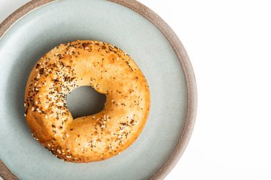 Beyaz arka planda seramik tabakta taze pişmiş tek bir simit..