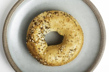 Beyaz arka planda seramik tabakta taze pişmiş tek bir simit..