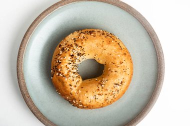 Beyaz arka planda seramik tabakta taze pişmiş tek bir simit..