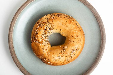 Beyaz arka planda seramik tabakta taze pişmiş tek bir simit..