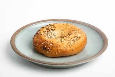 Beyaz arka planda seramik tabakta taze pişmiş tek bir simit..