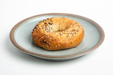 Beyaz arka planda seramik tabakta taze pişmiş tek bir simit..