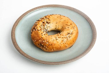 Beyaz arka planda seramik tabakta taze pişmiş tek bir simit..