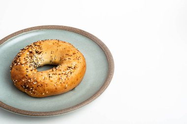 Beyaz arka planda seramik tabakta taze pişmiş tek bir simit..