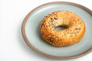 Beyaz arka planda seramik tabakta taze pişmiş tek bir simit..