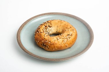 Beyaz arka planda seramik tabakta taze pişmiş tek bir simit..